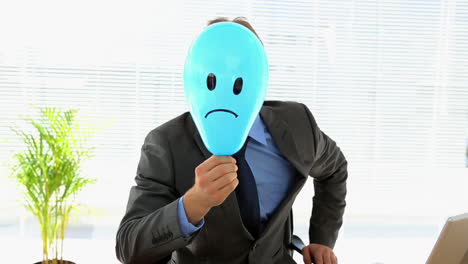 Grumpy-businessman-holding-sad-face-balloon-over-face