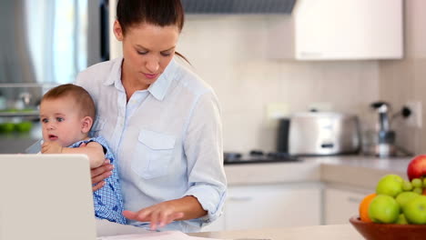 Pretty-mother-using-laptop-and-holding-baby