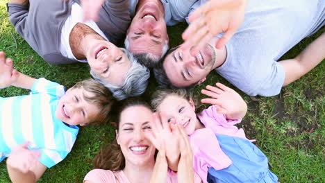 Extended-family-lying-in-the-park-together-smiling-up-at-camera
