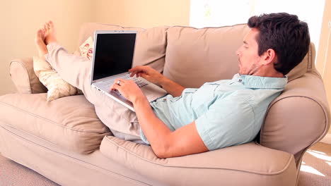 Man-lying-on-couch-typing-on-laptop