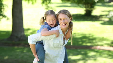 Happy-little-girl-getting-a-piggy-back-from-mother-in-the-park