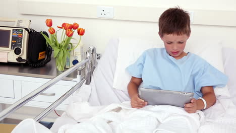 Little-sick-boy-sitting-in-bed-using-tablet-pc