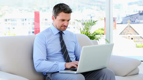 Businessman-typing-on-laptop-sitting-on-sofa