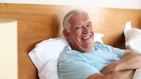 Senior-man-lying-in-bed-smiling-at-camera