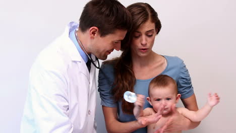 Pretty-mother-holding-baby-boy-while-pediatrician-listens-to-his-chest