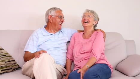 Senior-couple-sitting-on-sofa-chatting-and-hugging