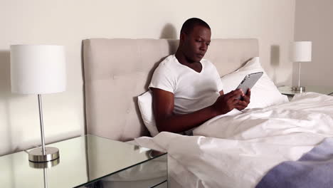 Man-sitting-in-bed-using-tablet