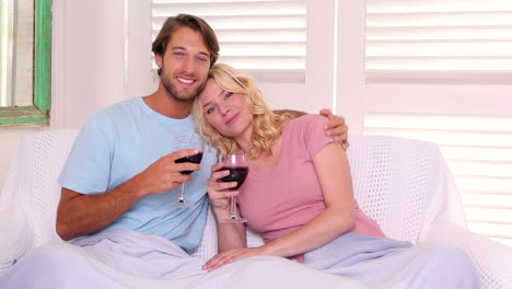 Couple-sitting-on-sofa-under-blanket-having-red-wine