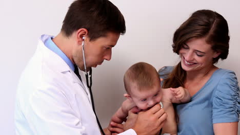 Pretty-mother-holding-baby-boy-while-pediatrician-listens-to-his-chest