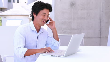 Hombre-Asiático-Usando-Una-Computadora-Portátil-Y-Contestando-Su-Teléfono