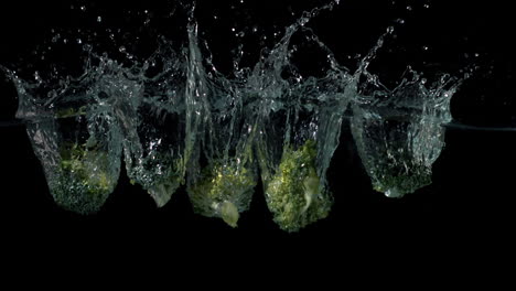 Broccoli-pieces-falling-in-water-on-black-background