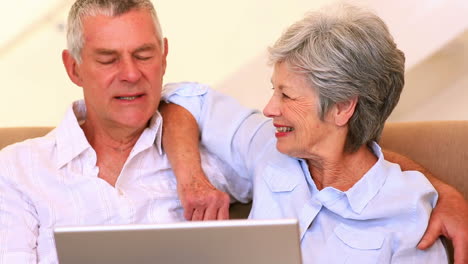 Happy-senior-couple-sitting-on-couch-using-laptop