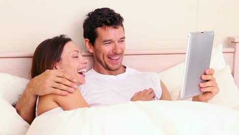 Couple-lying-in-bed-using-digital-tablet