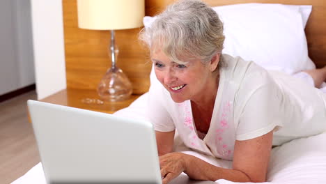 Senior-woman-lying-on-bed-using-laptop