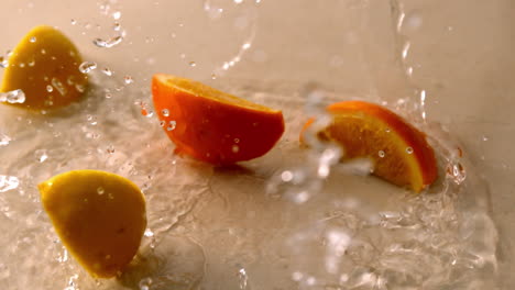 Orange-and-lemon-pieces-falling-on-wet-white-surface