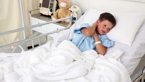 Little-sick-boy-sitting-in-bed-holding-his-neck