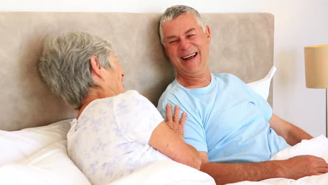 Happy-senior-couple-lying-in-bed-chatting