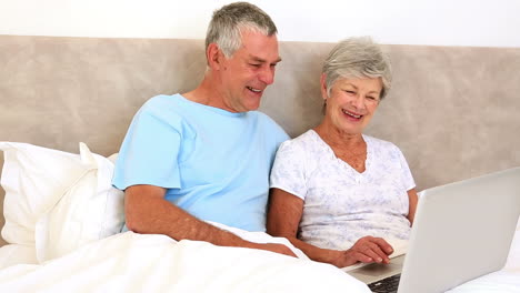 Happy-senior-couple-sitting-in-bed-using-laptop