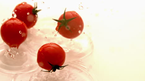 Tomates-Cherry-Cayendo-Sobre-Una-Superficie-Blanca-Húmeda