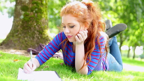 Pretty-young-student-lying-on-the-grass-making-notes-