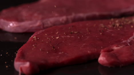 Beef-steaks-on-black-surface-being-seasoned