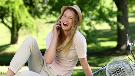 Pretty-girl-talking-on-smartphone-beside-her-bike-in-the-park