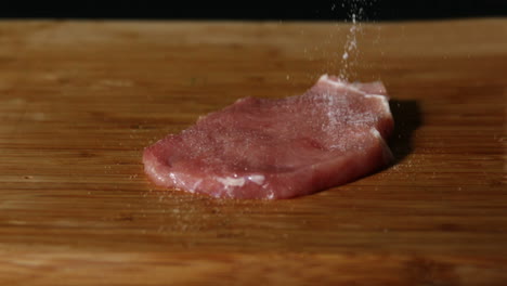 Pork-chop-being-seasoned-on-wooden-table
