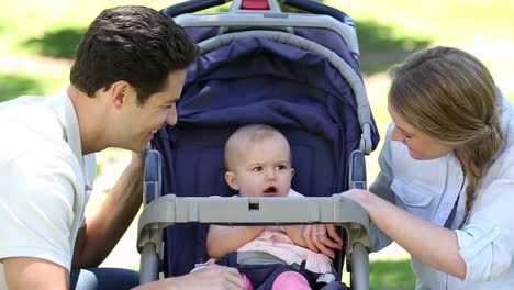 Happy-parents-tending-to-baby-girl-in-pram-in-the-park