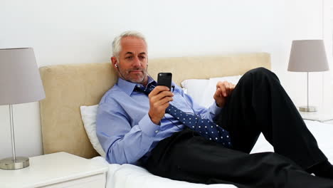 Businessman-lying-on-his-bed-listening-to-music