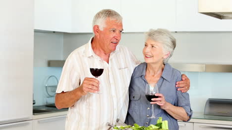 Senior-couple-preparing-a-healthy-salad-while-drinking-red-wine