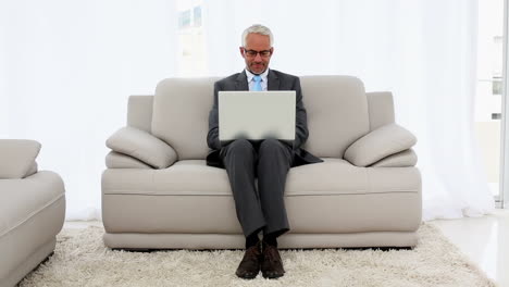 Smiling-businessman-using-laptop-on-the-couch