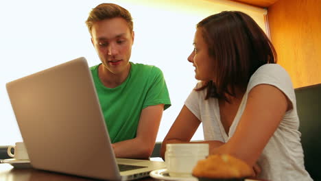 Friends-chatting-in-the-canteen-over-coffee-using-laptop