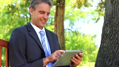 Businessman-sitting-on-park-bench-using-his-tablet