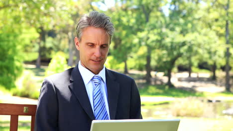 Businessman-sitting-on-park-bench-using-his-laptop