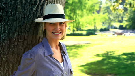 Smiling-woman-leaning-against-a-tree