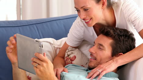 Happy-couple-relaxing-on-the-couch-looking-at-tablet-pc