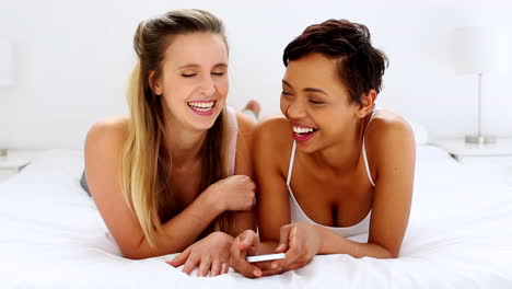 Zwei-Hübsche-Freundinnen-SMS-Auf-Dem-Smartphone-Auf-Dem-Bett-Liegend