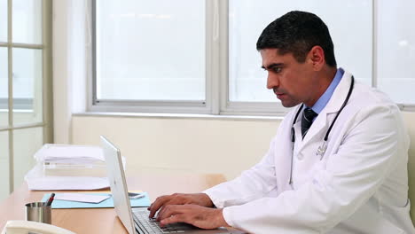Doctor-sitting-at-desk-typing-on-laptop