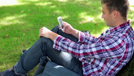 Hübscher-Junger-Student-Sitzt-Auf-Dem-Gras-Und-Schreibt-Eine-SMS
