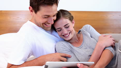 Happy-couple-lying-on-bed-using-tablet-together