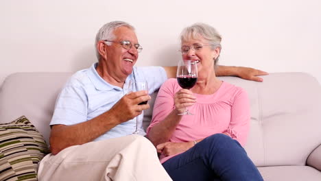 Senior-couple-sitting-on-sofa-drinking-red-wine
