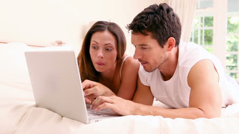 Glückliches-Paar,-Das-Zusammen-Auf-Dem-Bett-Liegt-Und-Einen-Laptop-Benutzt