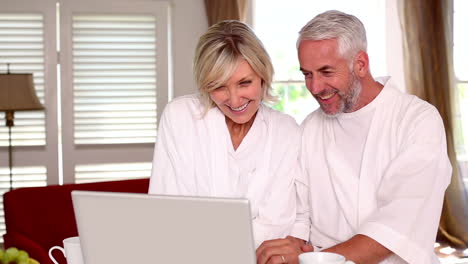 Una-Pareja-Feliz-Usando-Una-Computadora-Portátil-Juntos-En-Batas-De-Baño