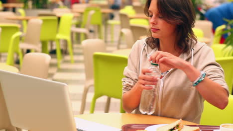 Brunette-student-studying-and-drinking-water-in-canteen