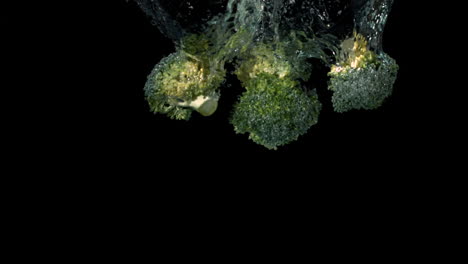 Broccoli-florets-falling-in-water-on-black-background