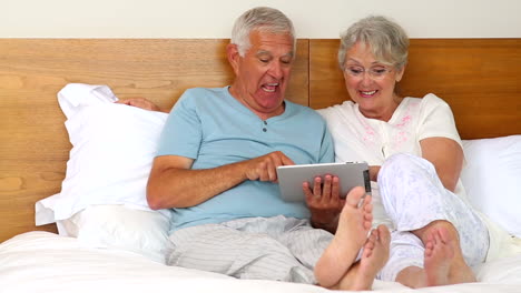 Senior-couple-sitting-on-bed-using-tablet