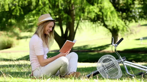 Pretty-girl-reading-beside-her-bike-in-the-park