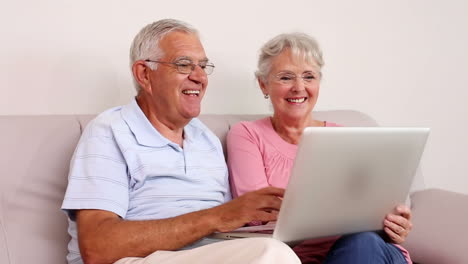 Senior-couple-sitting-on-sofa-using-laptop