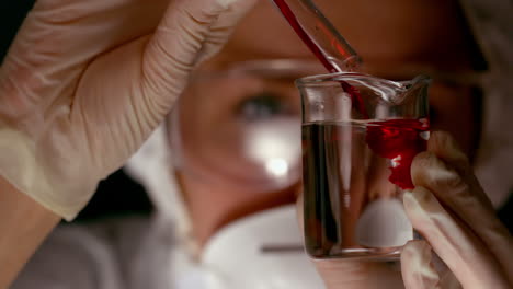 Scientist-pouring-red-chemical-into-beaker