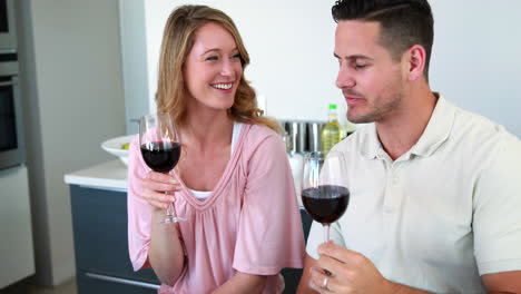 Happy-couple-smiling-at-the-camera-toasting-with-red-wine